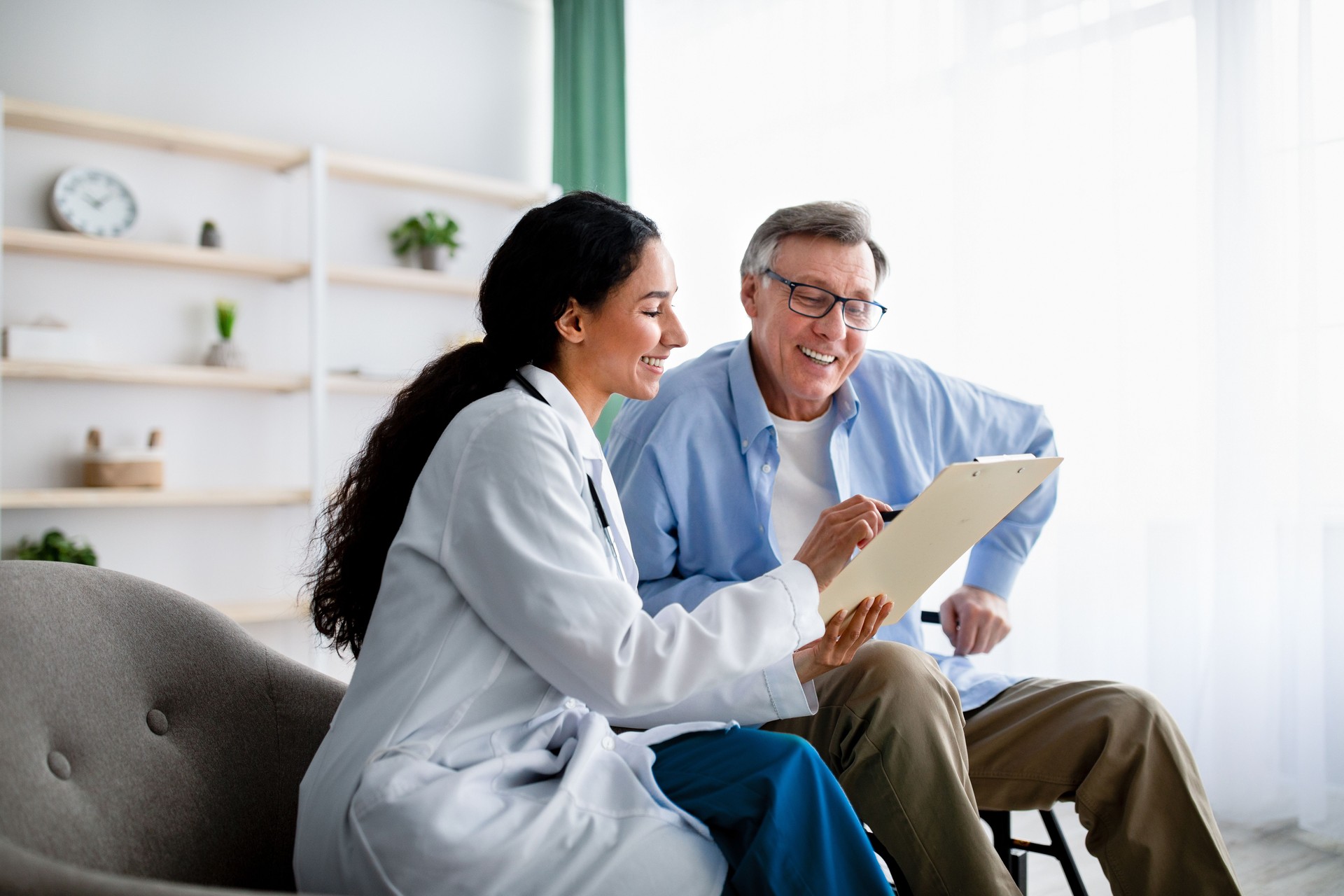 Young doctor asking senior impaired male patient in wheelchair to sign insurance policy at home